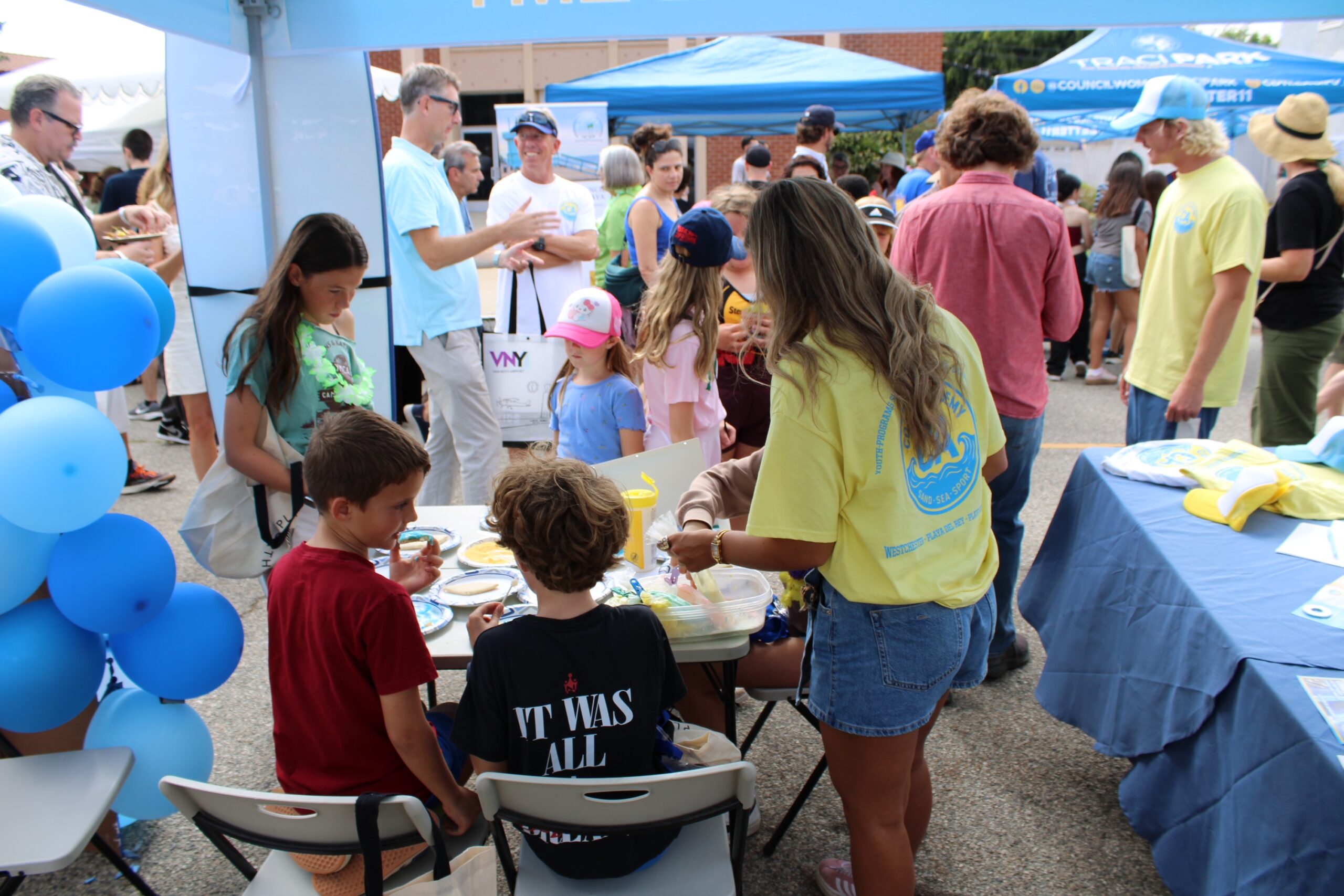 Children participate in a hands-on activity at a community event, engaging with adults and other kids while enjoying food and fun.